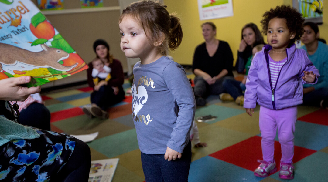 Toddlers crowding around librarian to see book during storytime