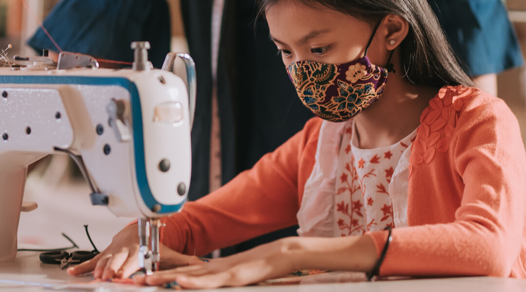 Masked teenager using a sewing machine