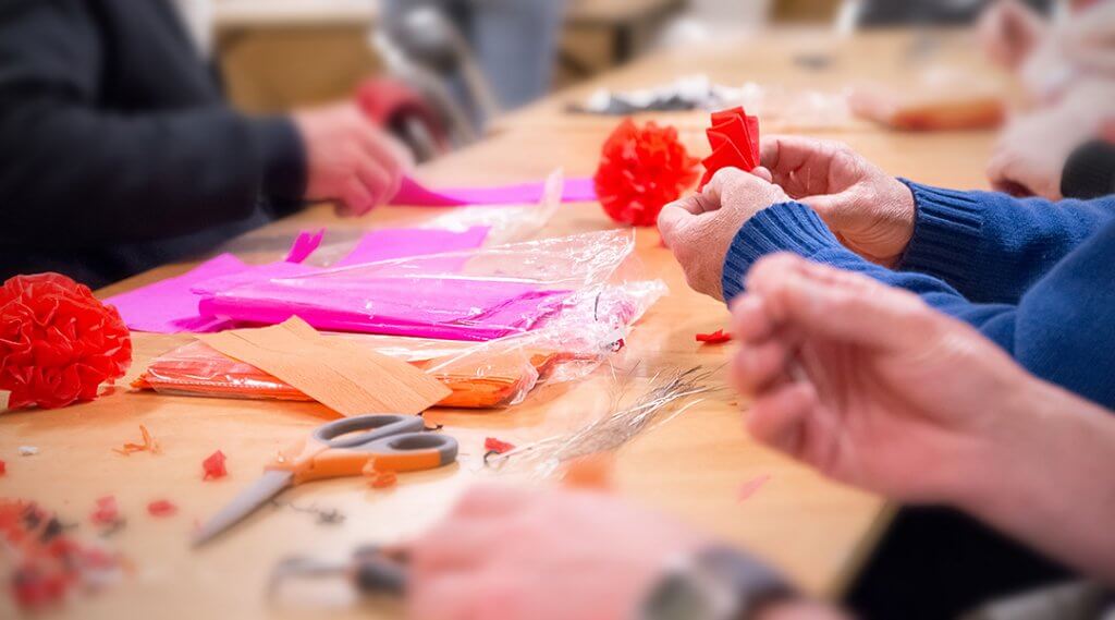 Photo of hand making red, magenta and orange colored crepe paper decorations.