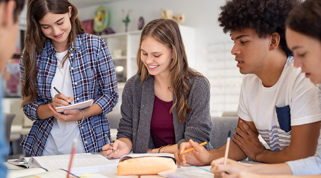 Group of teens crowded around table with paper and pens out