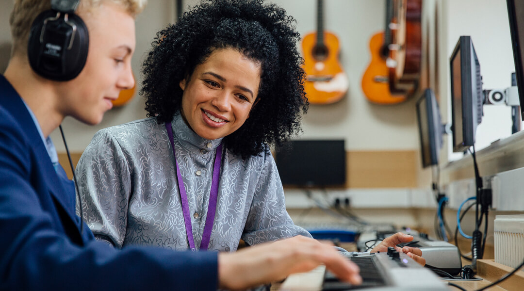 Two teens in a music lab, one playing the keyboard