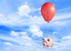 piggy bank floating on a red balloon with a blue sky in the back drop.