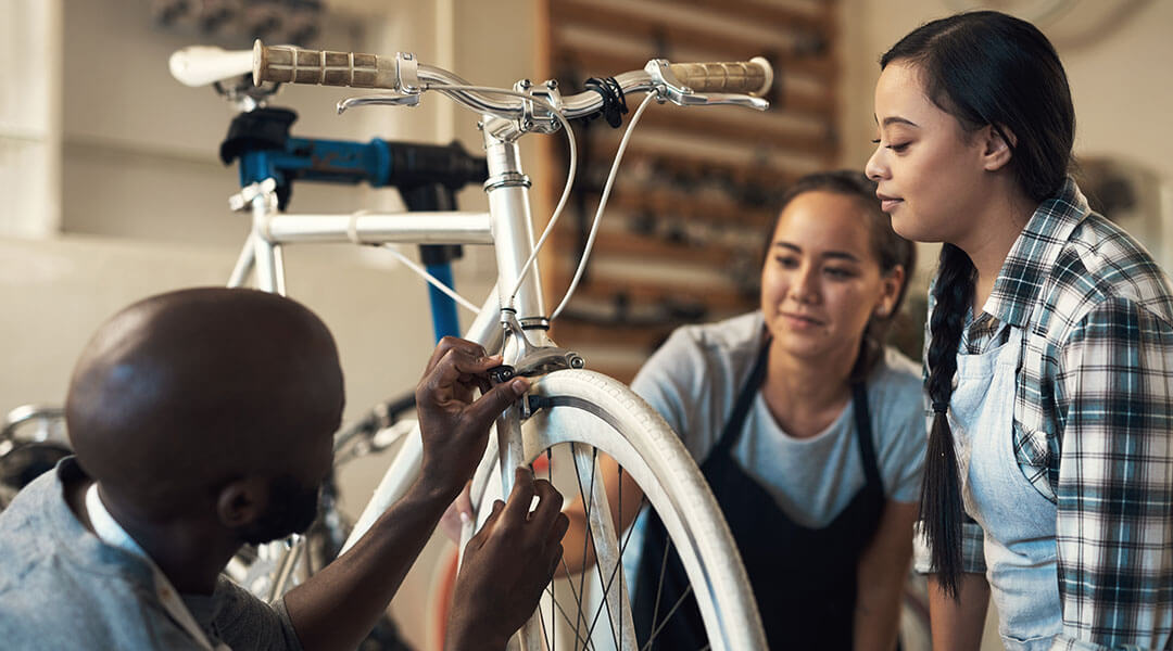 A person repairs a bike while two others look on