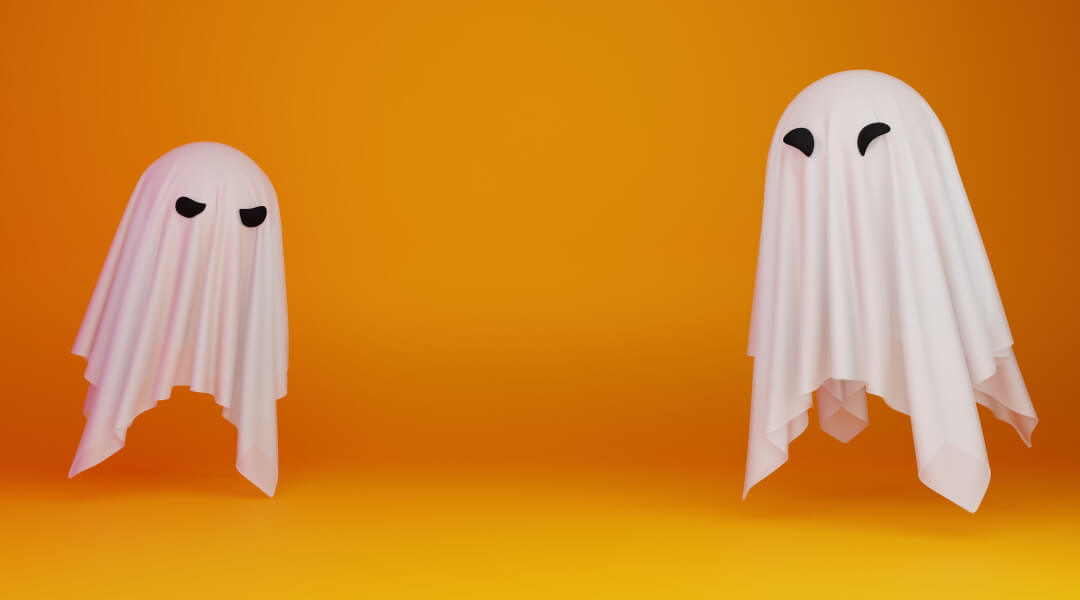 Two traditional white sheet ghosts floating in front of an orange background