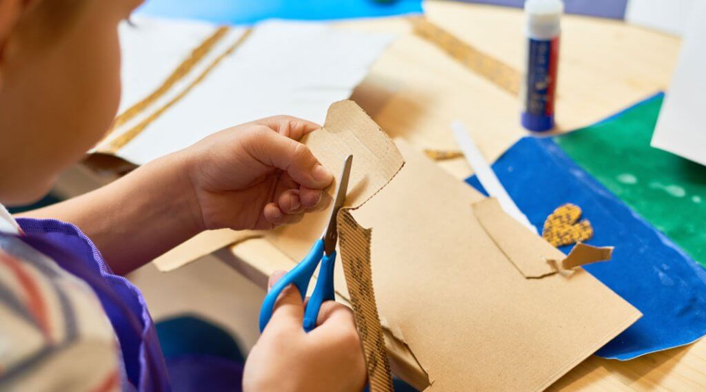 Child cutting cardboard as part of a craft project.