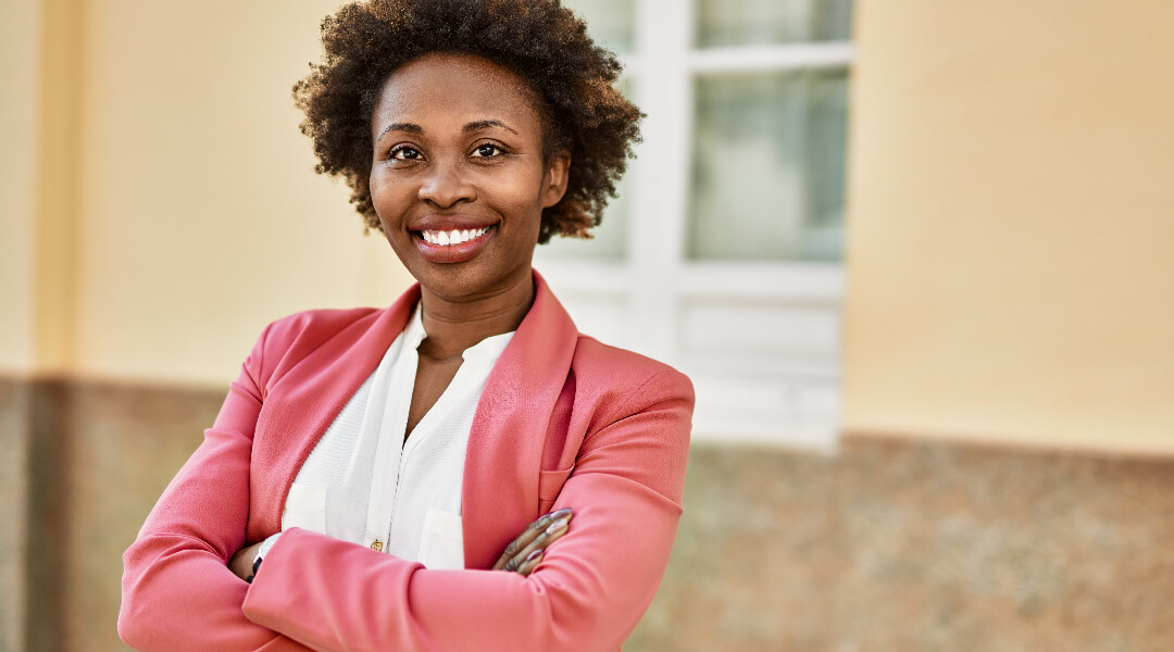 Woman posed with arms crossed, smiling in front of a building