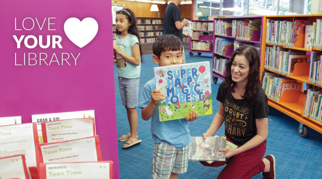 caregiver and child holding up a book in Children's Department with text reading "Love You Library"