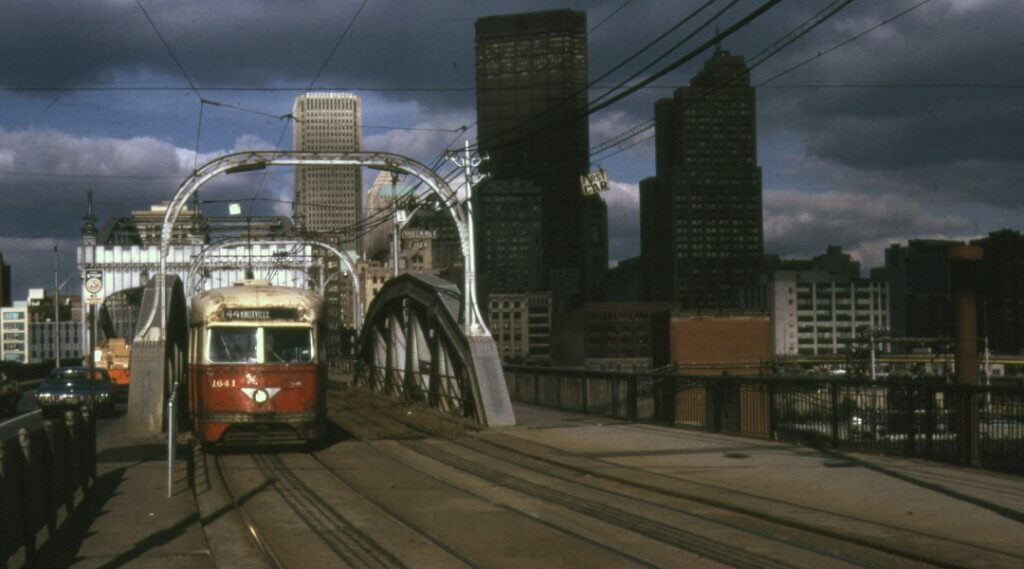 Vintage photo of a white and red trolley crossing a Pittsburgh bridge.
