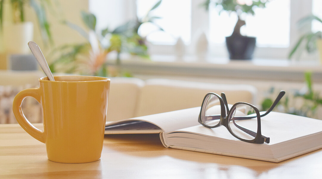 Steaming mug next to book and reading glasses