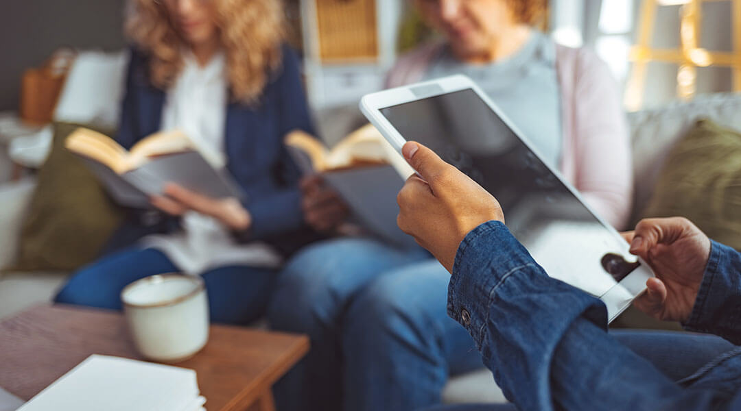 Small group of people with a mixed age range sitting at a table, discussing and reading books together.