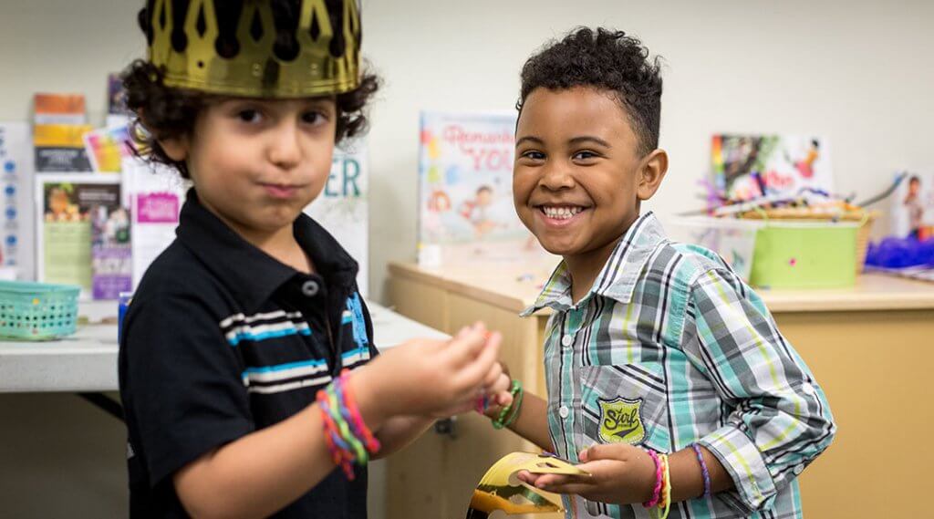 Two kids smile with their gold paper crowns