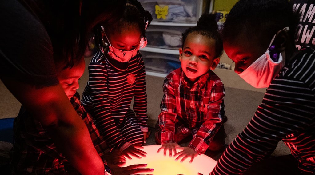 Four young children and an adult explore a glowing red light in the children's area of the library