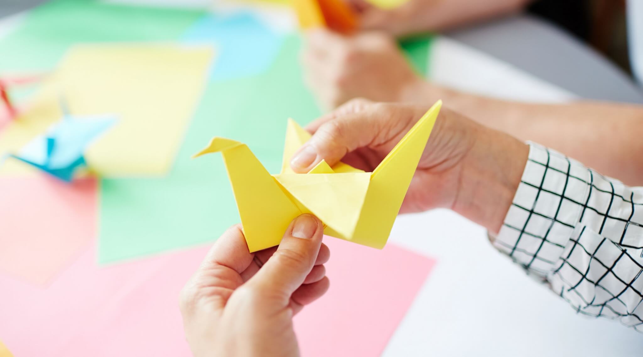 Human hands folding sheet of yellow paper while making origami bird