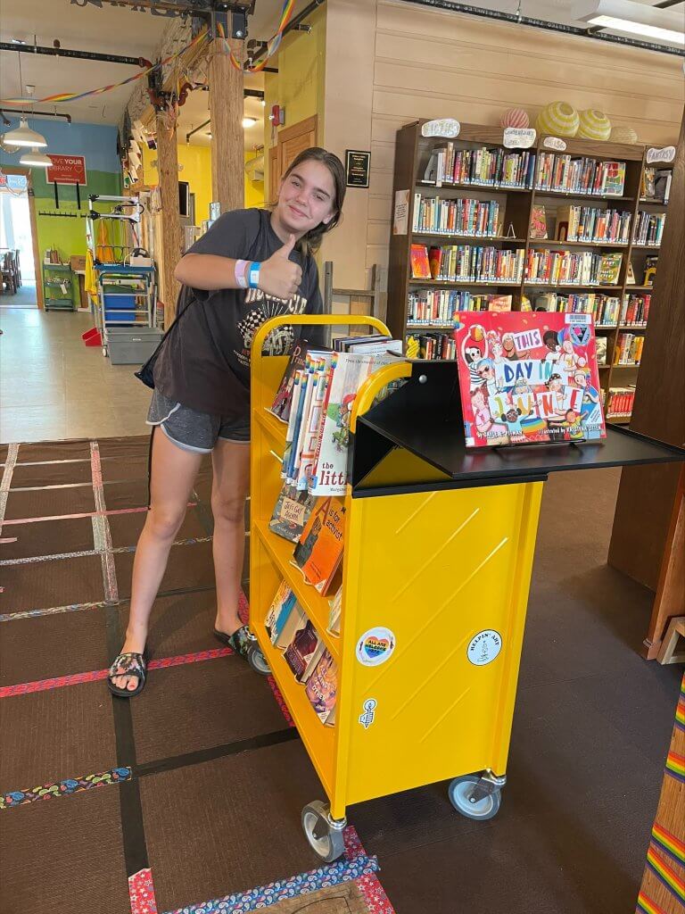 A person poses with the bright yellow book cart