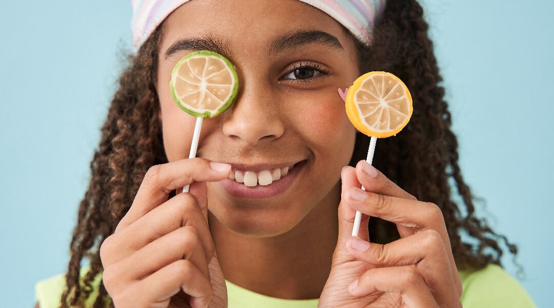 A tween holds up two lollipops that look like lemon and lime slices.