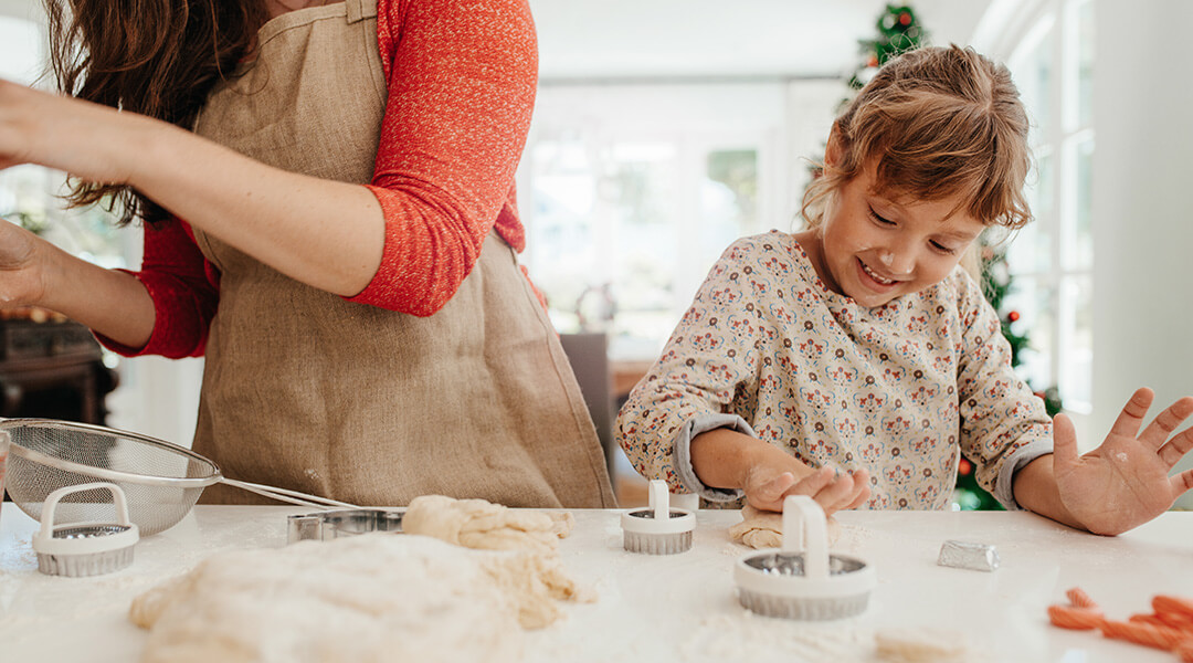 An adult and young child make holiday cookies using cookie cutters at a table.