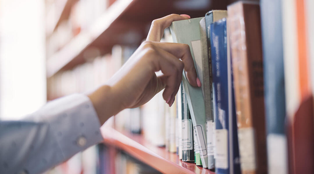 Close up of a hand retrieving a book from a library shelf.