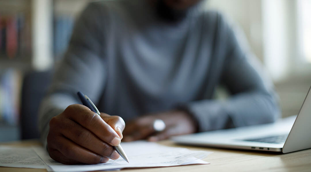 Close up of a person taking notes while using a laptop.