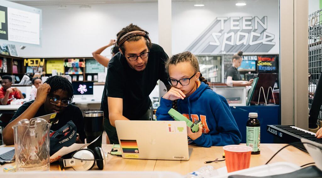 Two teenagers receive help on a laptop in the library's Teen Space.
