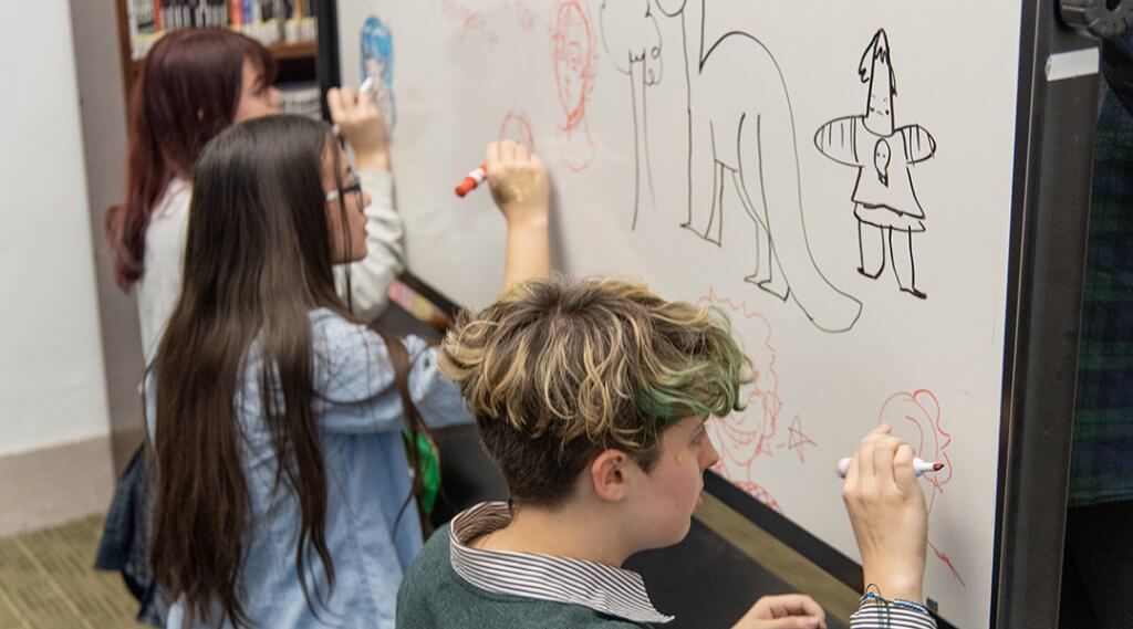 Three teenagers drawing on a whiteboard.