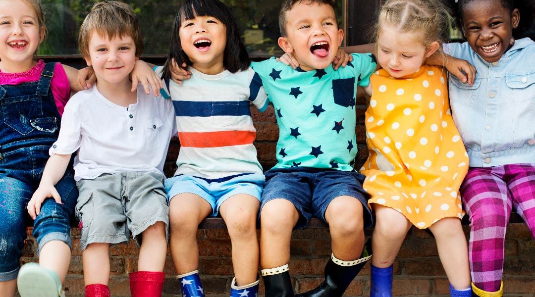A row of toddlers, smiling, with their arms around one another