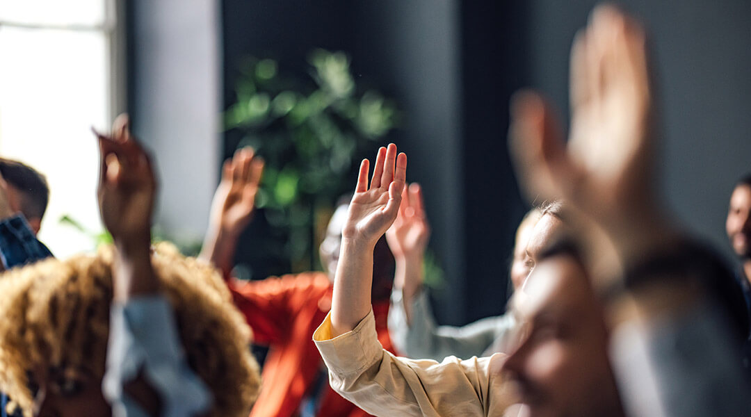 Group of people sitting on a seminar. They have their hand raised.