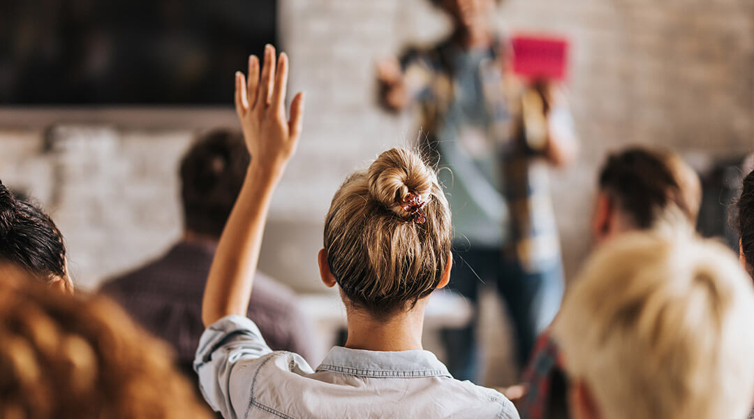 Rear view of casual businesswoman raising her hand to ask the question on education event in a board room.