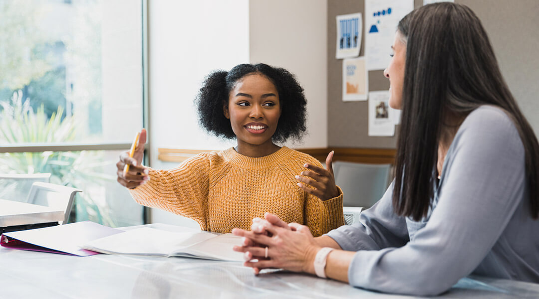 A young adult gestures as she speaks to an adult in a one-on-one meeting.