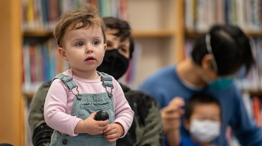 A toddler holds a shaker egg during a library storytime.