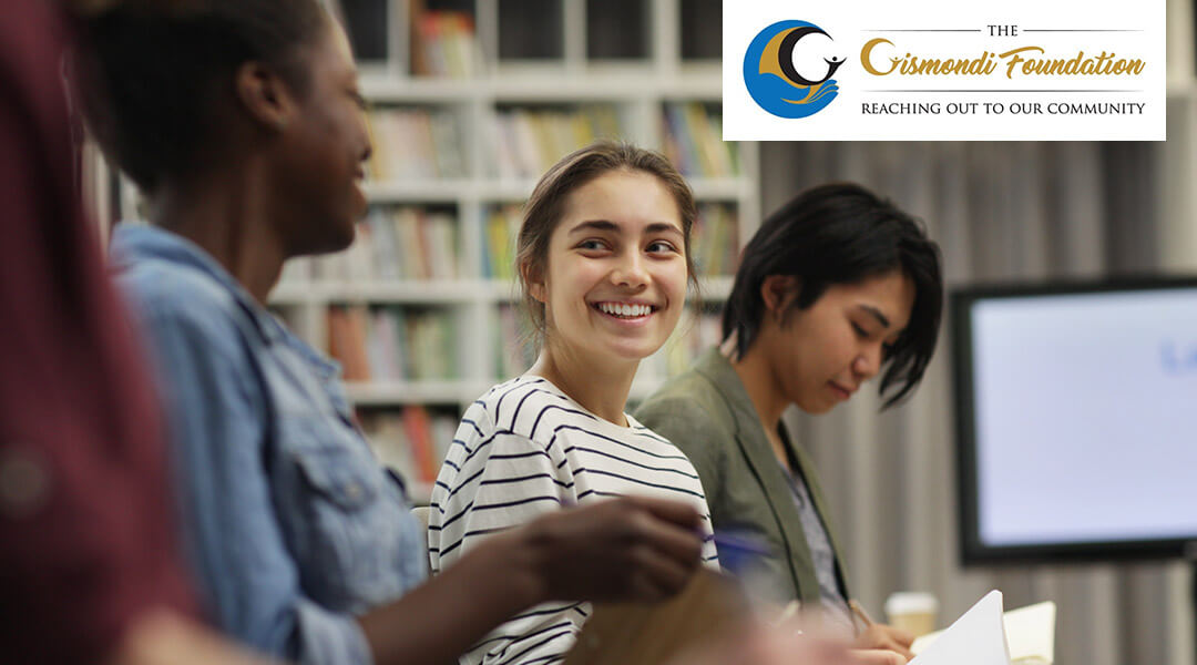 Three teens smiling and talking in the library with the Gismondi Foundation logo in the upper right corner.