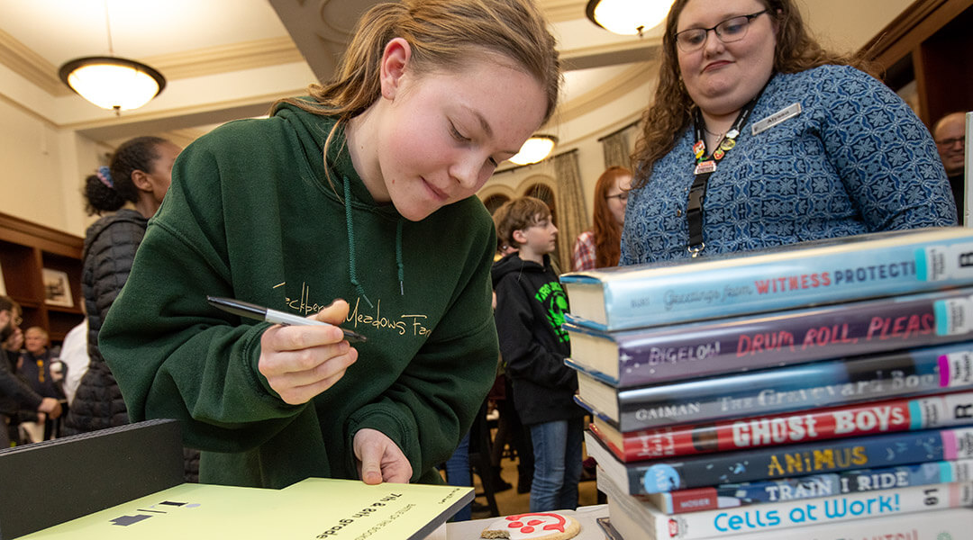 A teen signs the Teen Battle of the Books trophy.