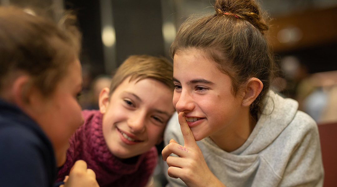 Three teens smile and whisper together.