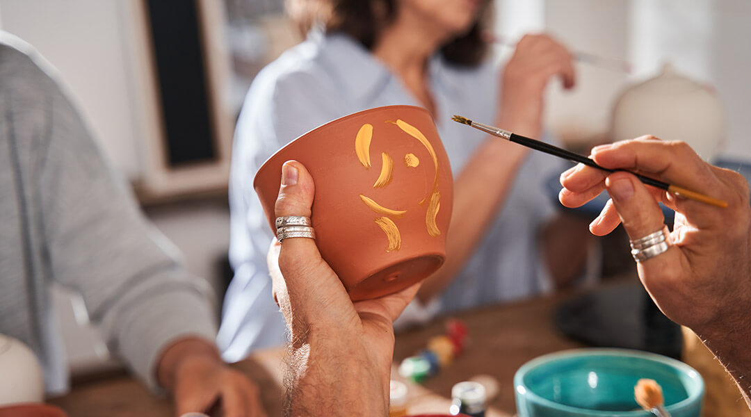 A person holding clay pot and brush paints patterns on it during a group class.