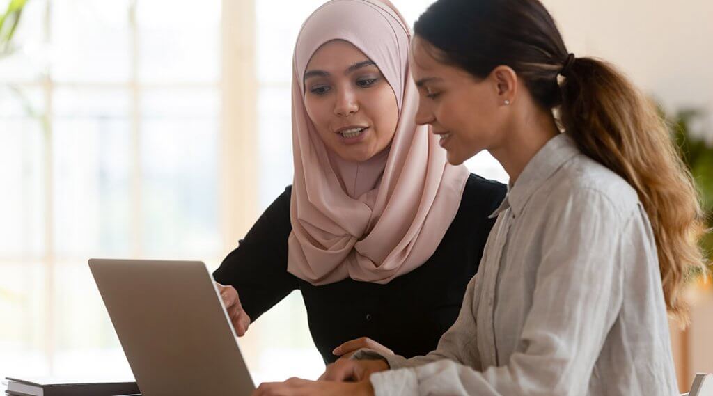 Two young women work together at a laptop.