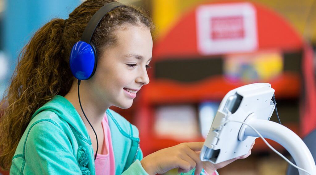 A child wears headphones and uses a library tablet.