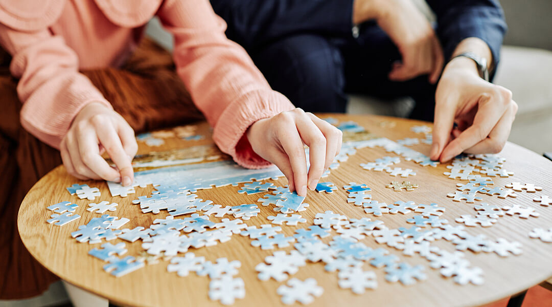 Close-cropped shot of two people working on a jigsaw puzzle together.