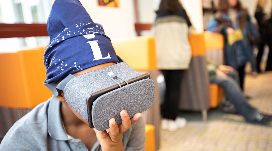 A teenager holds a VR headset to their face.