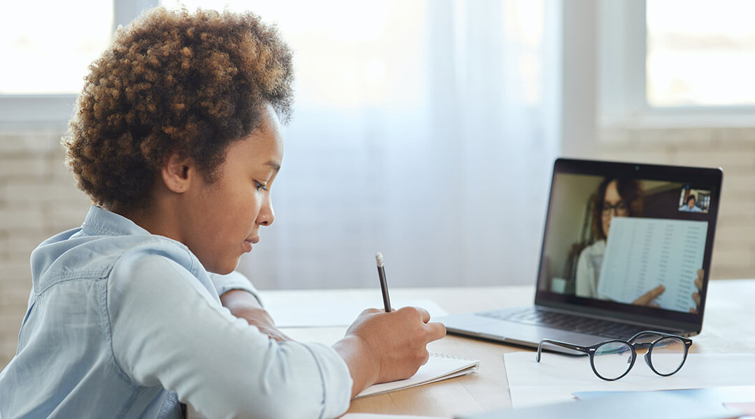 A child takes notes during a virtual study session with a tutor.