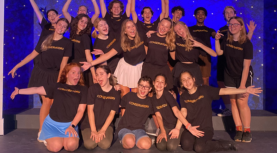 A group of teenagers wearing t-shirts that read 'conservatory' posing on a stage.