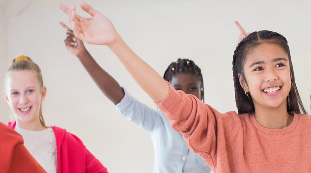 Three school-age children raise their hands mid-dance.