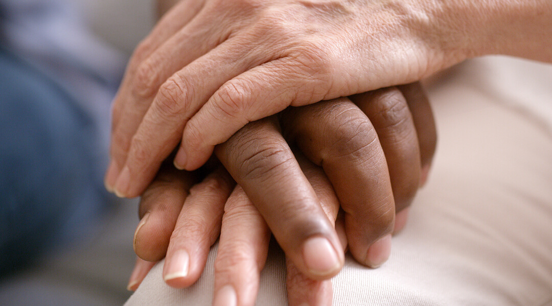 A close photo of one person gently clasping another's hands.