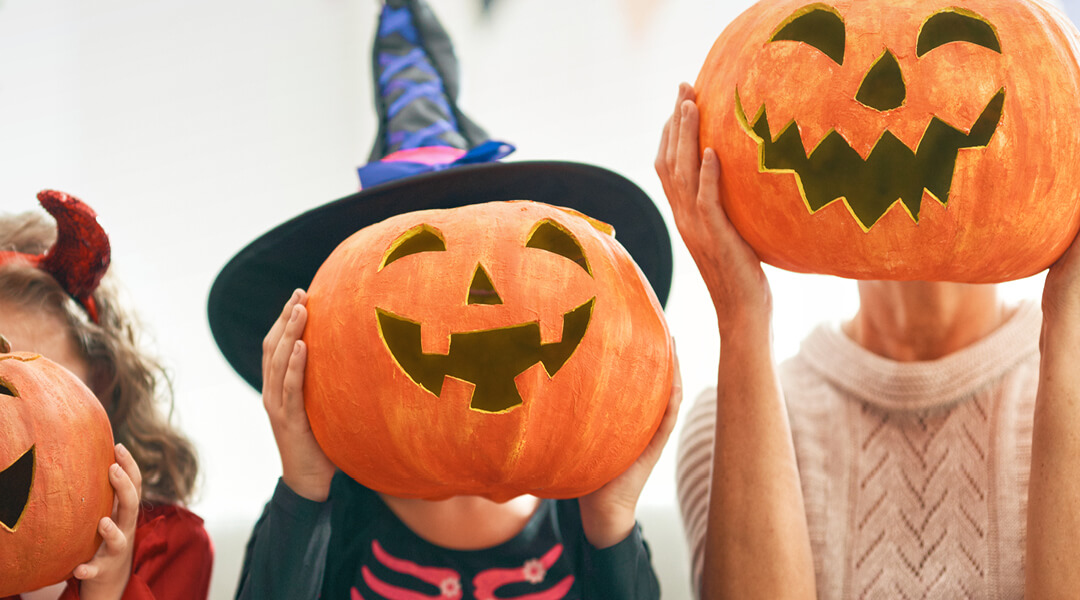 Children pose with pumpkins painted to look like jack-o-lanterns in front of their faces.