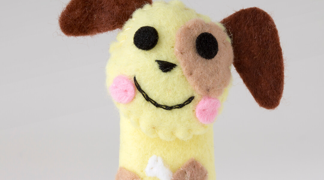 A felt finger puppet that looks like a smiling dog.