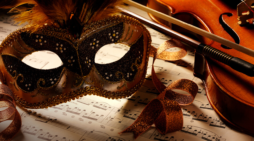 An ornate mardi gras mask and a violin sit atop sheet music.