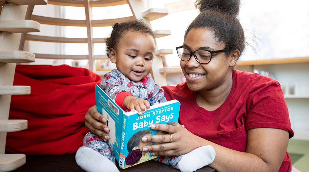 An adult caregiver reading a board book to a baby