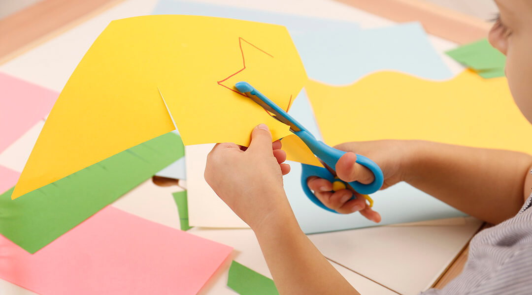 A child cutting color paper with scissors at table.