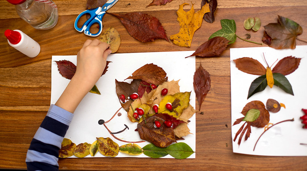 Child applying leaves using glue while doing arts and crafts.