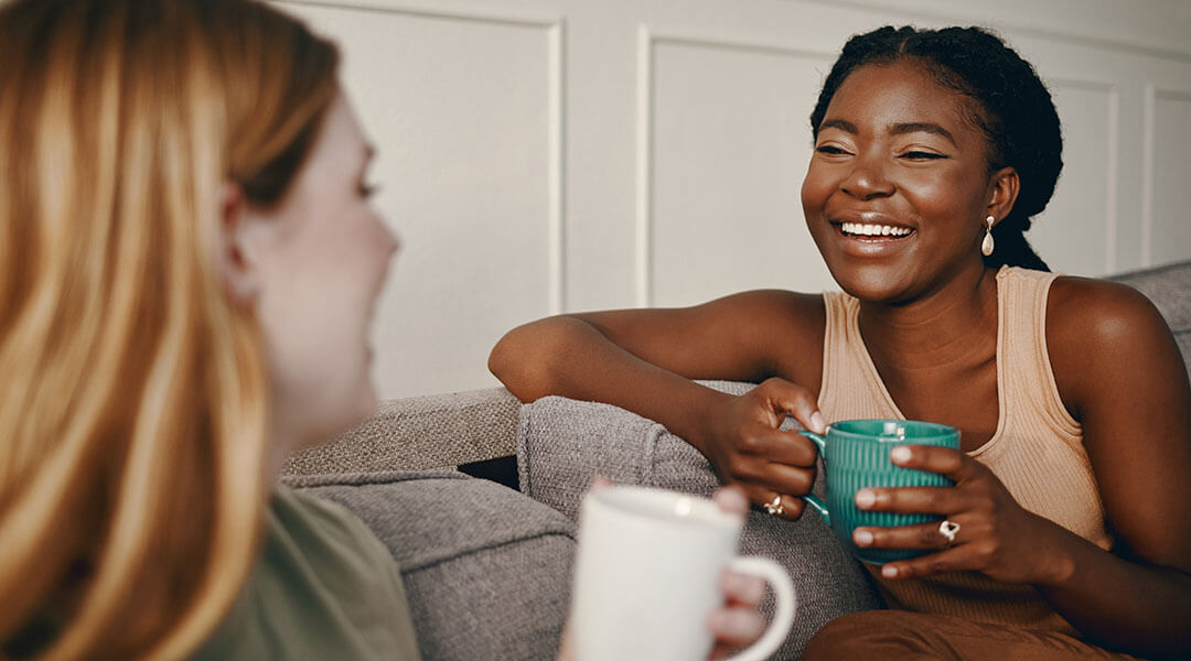 Two young adults chat on a couch while drinking coffee.