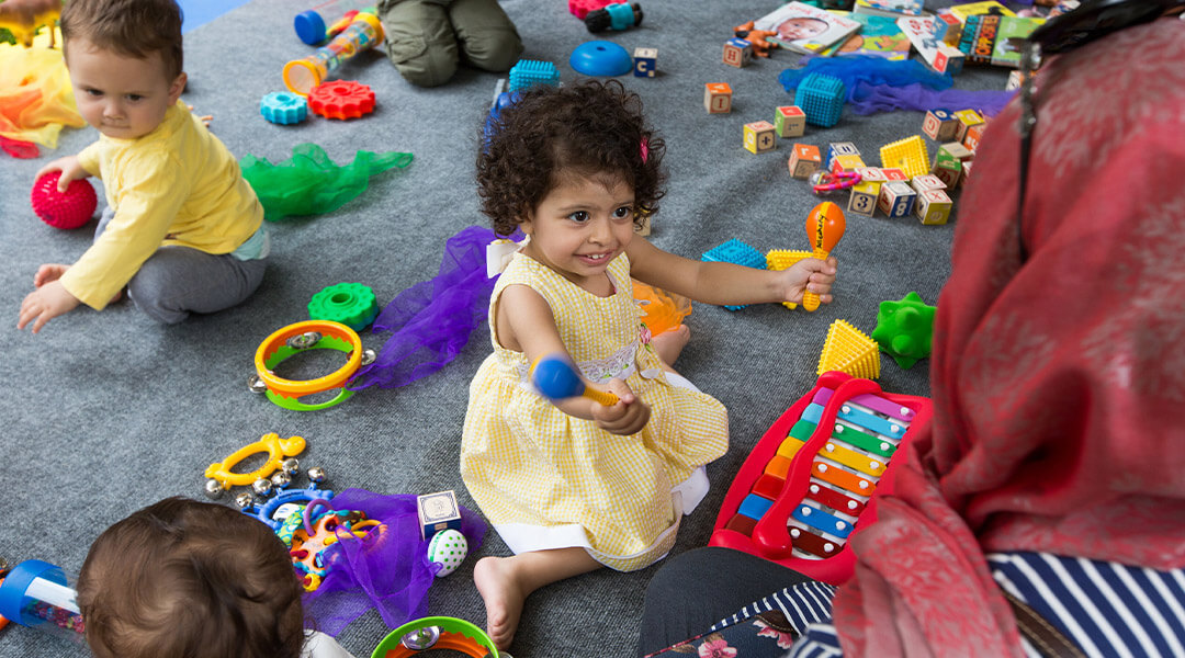 Babies and toddlers play with a spread of toys on the library floor.