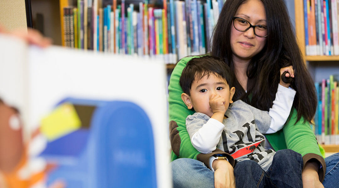A toddler cuddles on a caregivers lap during storytime.